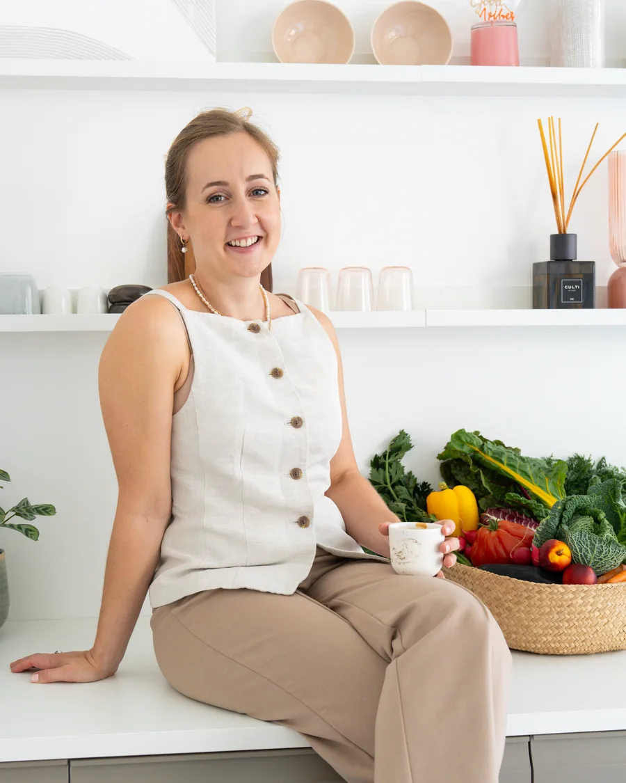 Jelina Linder sitzt mit einer Tasse auf der Küchentheke, daneben ein Korb mit frischem Gemüse