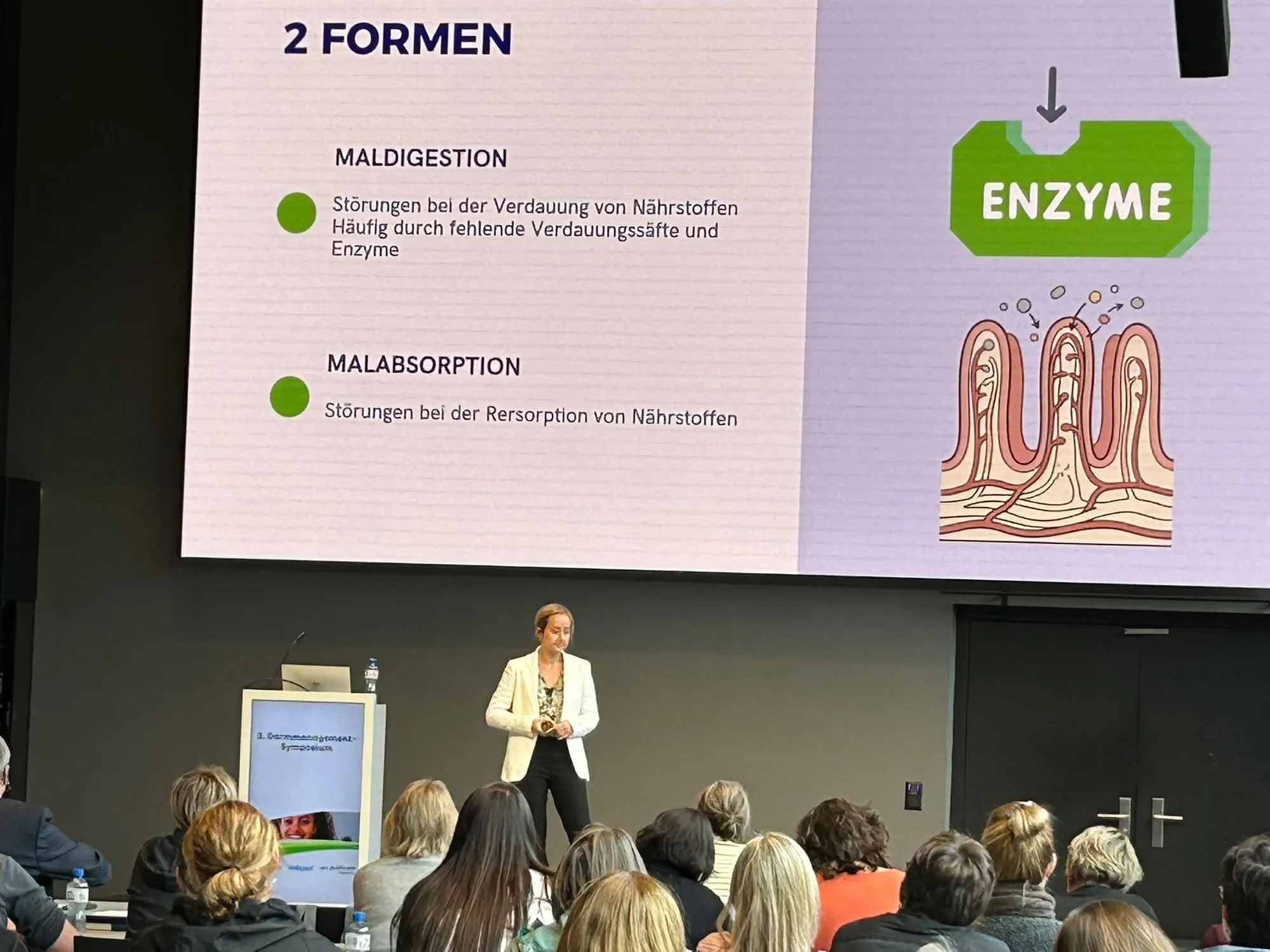 Jelina Linder spricht vor vollem Saal, auf der Leinwand eine Folie zu Maldigestion, Malabsorption und Enzymen